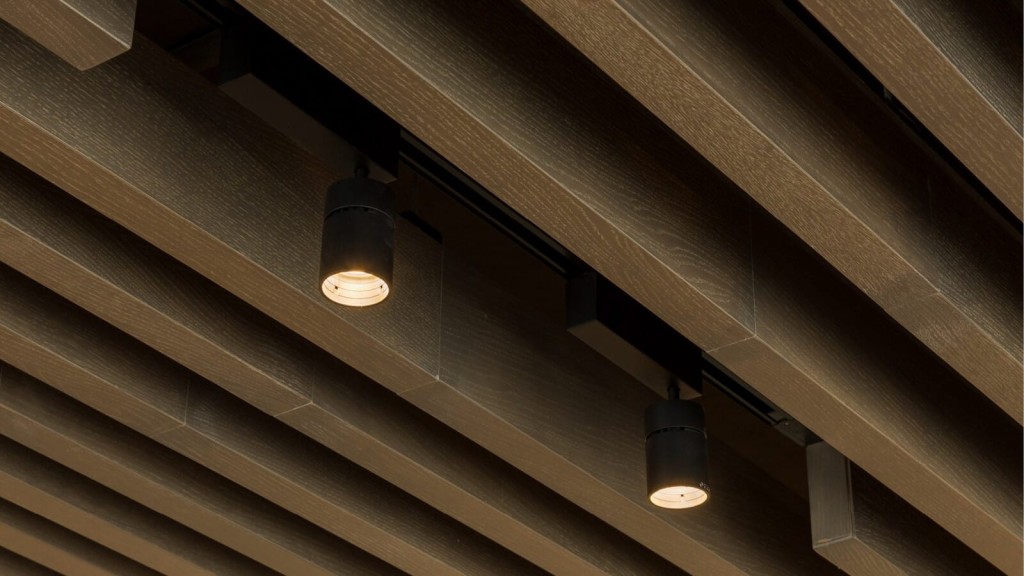 Close-up of modern track lighting with cylindrical black pendants against a textured wooden ceiling, providing a warm and sophisticated ambiance.