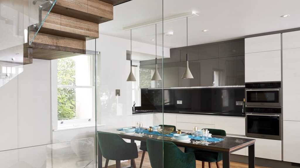 Modern kitchen with white cabinets, black countertops, and built-in appliances, complemented by a dining area with a wooden table, green velvet chairs, and chic pendant lights.
