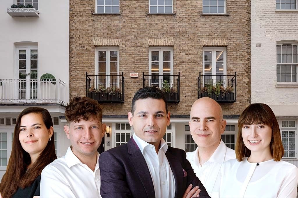 Team of five professional architects, with a balanced mix of genders, smiling confidently in front of classic London townhouses with brick facades and Juliet balconies, showcasing a blend of traditional and modern urban design.