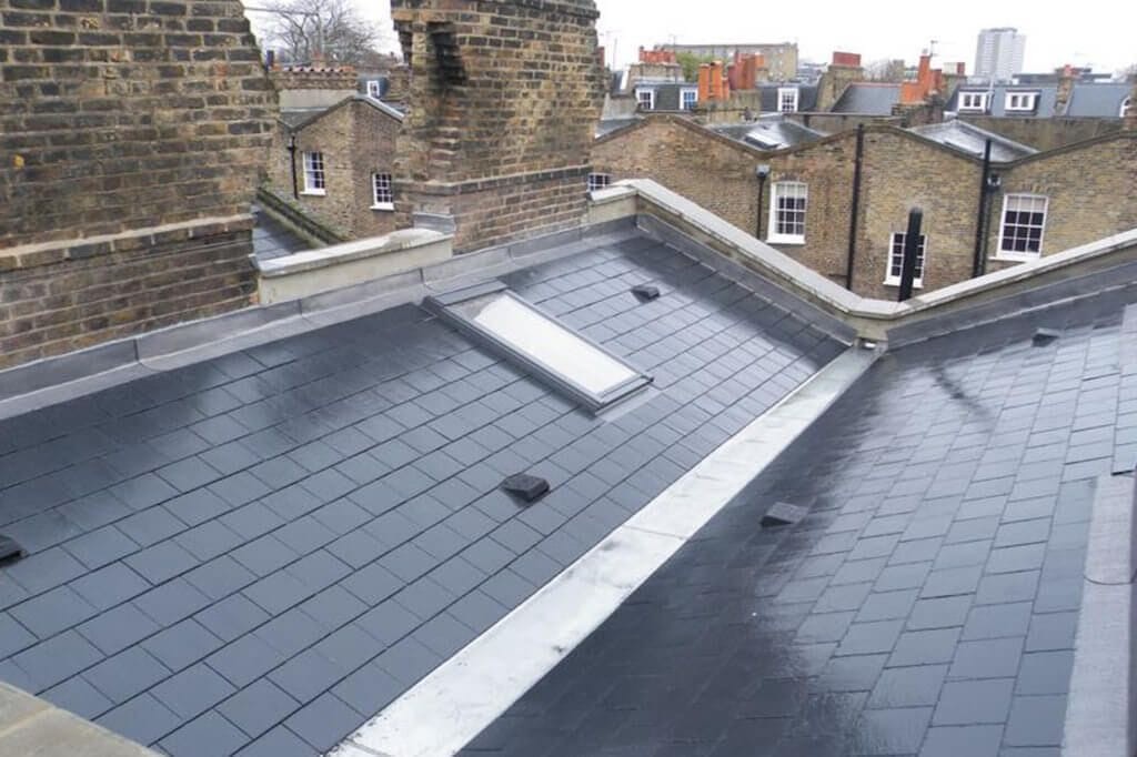 Newly constructed slate butterfly mansard roof with skylights, bordered by traditional brick chimneys, against a backdrop of a classic London skyline with diverse residential architecture.