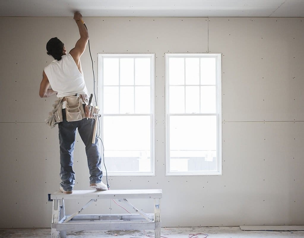Solo worker from a small contractor company in London working on the interior renovation of a small property in the city standing on work platform with a tool belt working on sanding the white ceiling