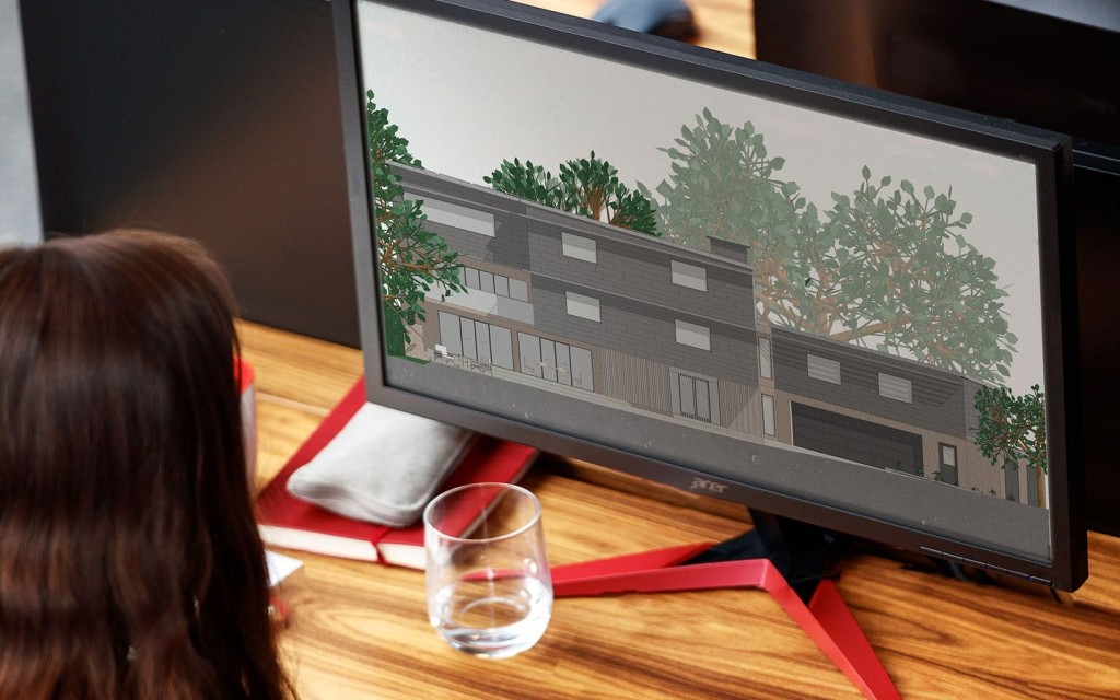 Architect viewing a digital rendering of a modern residential building on a computer screen. The design includes multiple floors, large windows, and surrounding greenery, illustrating the use of advanced 3D BIM software tools in planning and meeting minimum space standards for new housing developments.