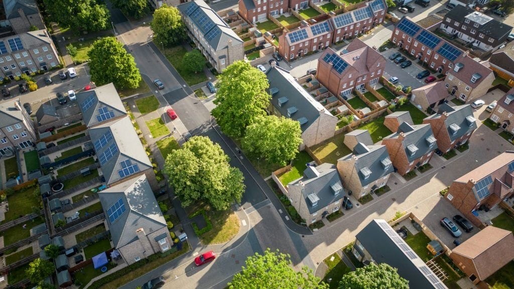 Aerial view of a modern residential neighbourhood with newly built homes featuring solar panels on the rooftops, tree-lined streets, and neatly arranged gardens.