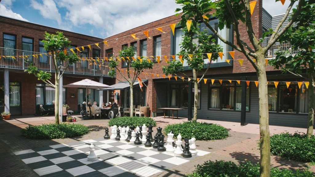 Residents enjoying outdoor courtyard with oversized chess set at contemporary care home facility.