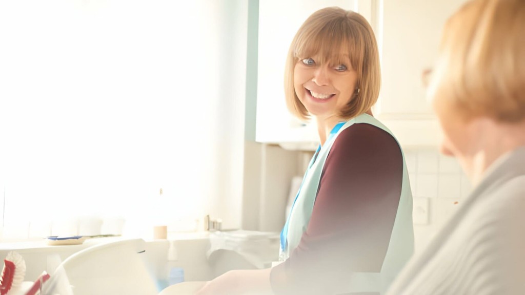 Smiling caregiver assisting senior woman in sunlit modern care home environment.