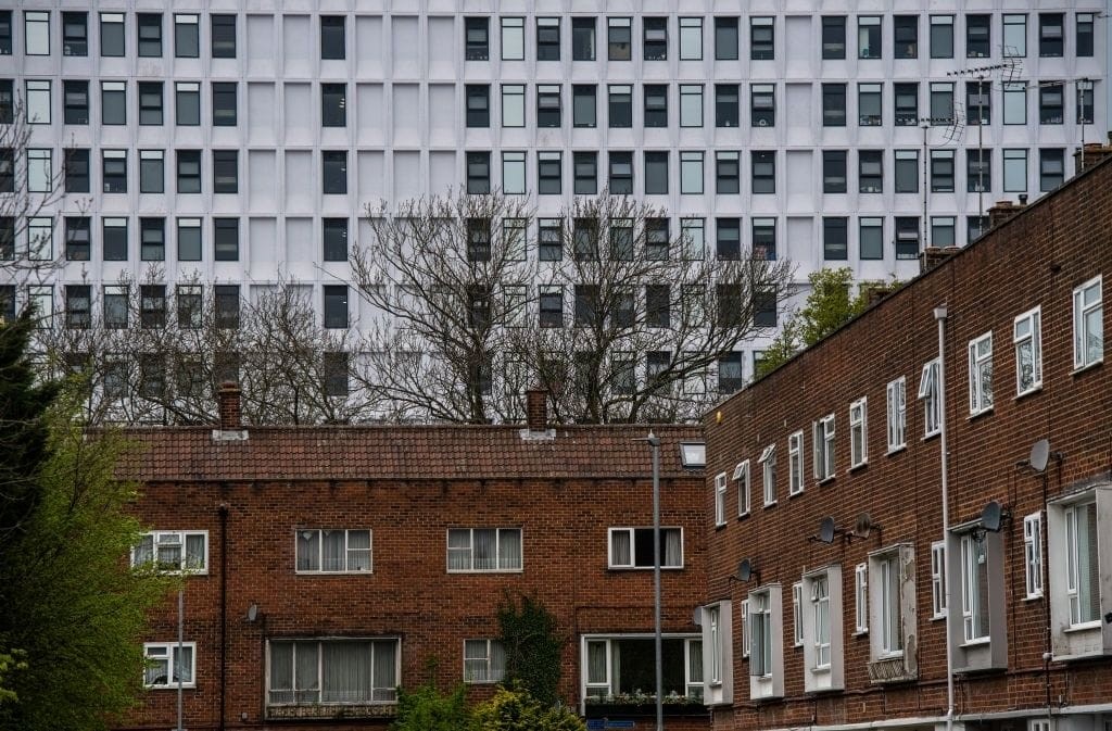 A row of mid-century red-brick residential buildings with satellite dishes on their facades, framed against the backdrop of a stark white modern office block with grid-like windows, highlighting the contrast between different eras of architecture influenced by changing Permitted Development Rights.