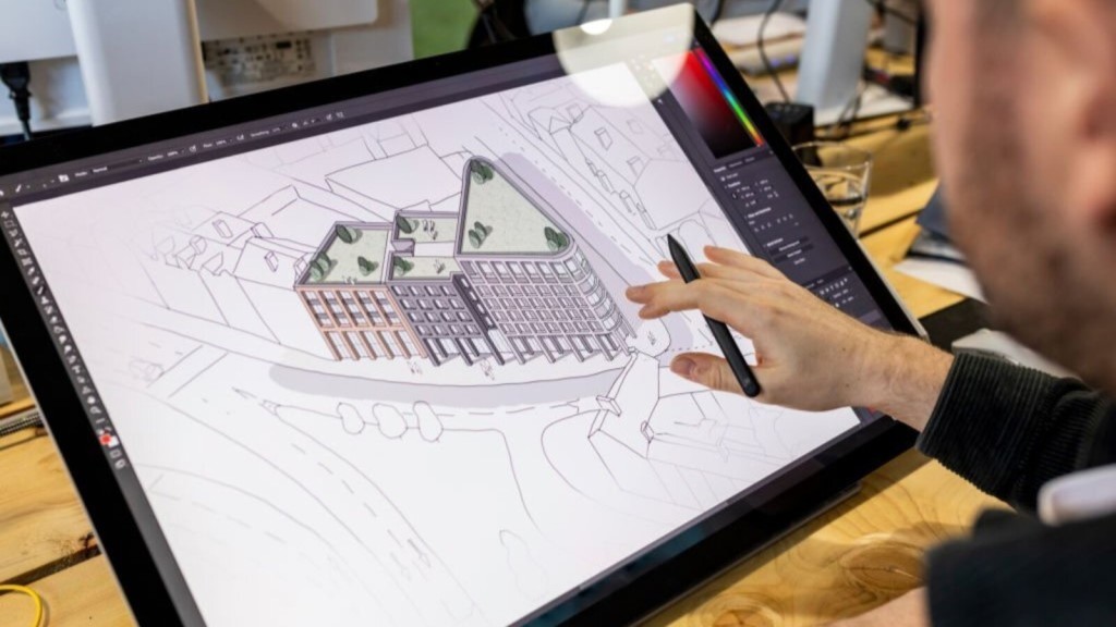 An architect uses a digital drawing tablet to design a modern residential building. The screen displays detailed architectural plans, including green roof spaces. This image represents the industry's response to updates in planning rules, showcasing modern technology in architecture and the focus on sustainable development.