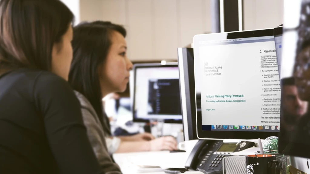 Planning professionals reviewing the August 2026 National Planning Policy Framework (NPPF) on a computer screen in an architecture office, with the document open to its plan-making policies and spatial development strategy section.