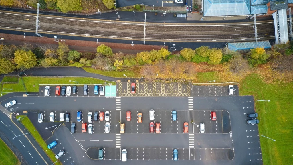 Aerial view of parking for a new housing development next to a railway station in the UK, with marked spaces, accessible bays and pedestrian crossings.