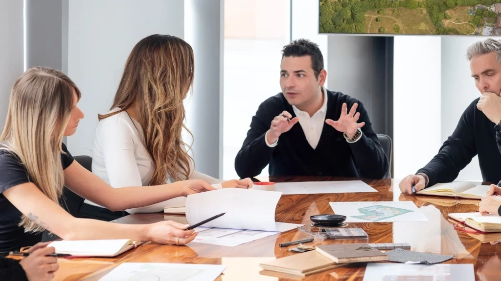 Architects and planning consultants discussing site plans and an aerial land survey during a development strategy meeting, reviewing the practical implications of the NPPF 2026 for planning and housing development in England.