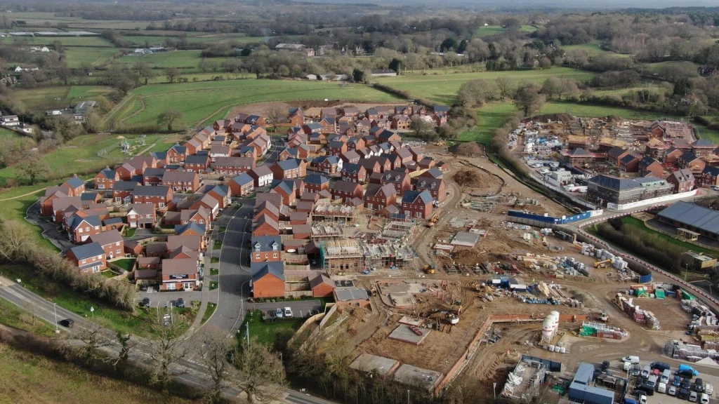 Aerial view of a large new-build housing development under construction beside completed homes and surrounding countryside, illustrating housing growth, land development and infrastructure delivery under the NPPF 2026.