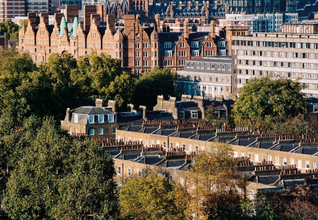 Aerial view of a traditional London street with rows of Victorian townhouses and distinctive terraced architecture, juxtaposed against a backdrop of modern buildings, highlighting the city's architectural diversity.