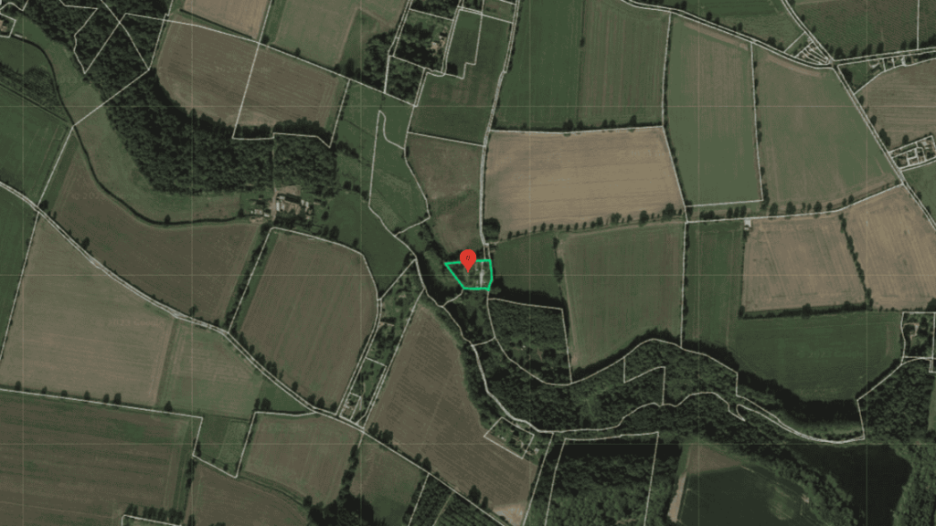 Aerial view of agricultural land with a red location marker pinpointing a specific area, showcasing a patchwork of fields and trees, indicative of rural land management and surveying.