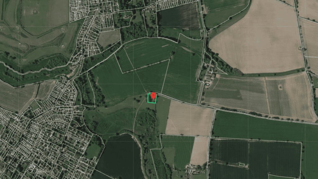 Drone view of a rural area with a clear demarcation between agricultural fields and residential development, featuring a red pin on a highlighted parcel of land, indicative of geographical analysis or real estate assessment.