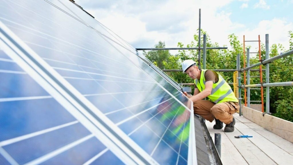 Skilled technician installing solar panels on a roof, demonstrating renewable energy solutions in action, with safety equipment and scaffolding in a lush green environment.
