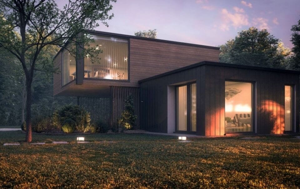 Modern countryside house at dusk featuring sleek design with large glass windows, a cantilevered upper story, and wooden cladding surrounded by lush greenery and soft landscape lighting.
