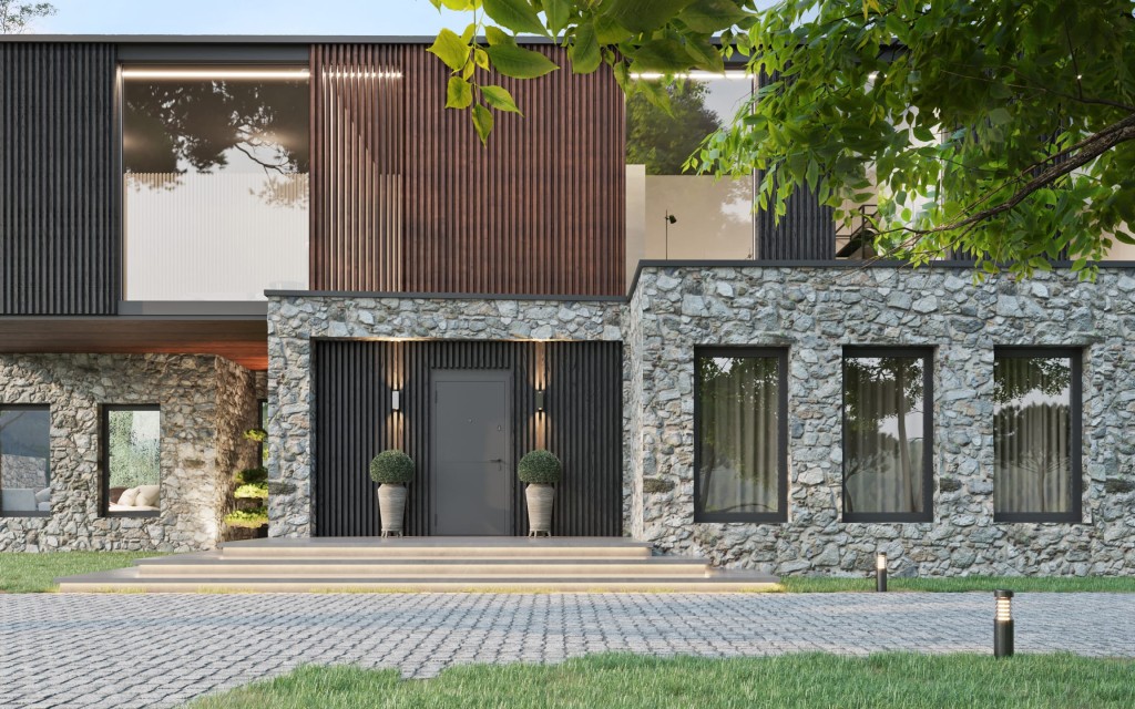 A modern countryside house with a stylish combination of dark wood cladding and natural stone walls, featuring tall vertical windows and a welcoming entrance flanked by potted topiaries, under the gentle shade of green trees.