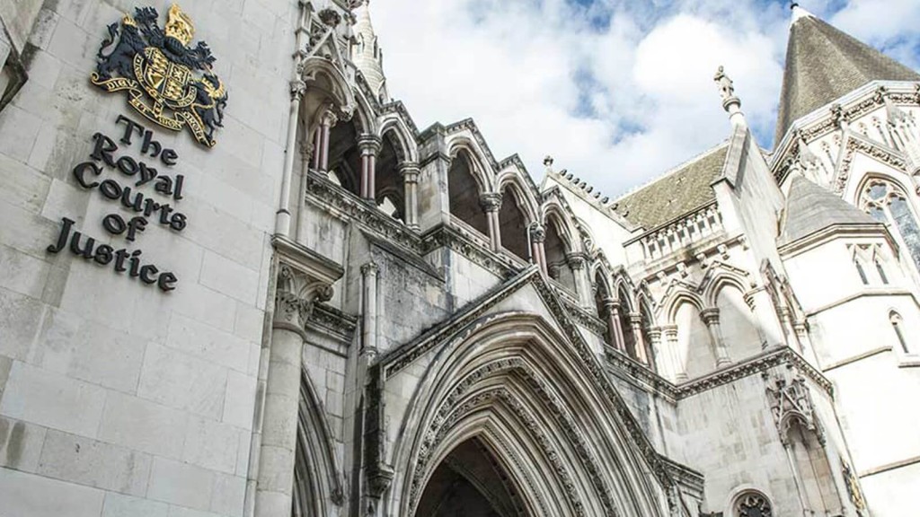 Facade of The Royal Courts of Justice in London, showcasing the gothic architecture and the building's sign with the UK royal coat of arms, symbolising the judicial authority and legal proceedings in England.