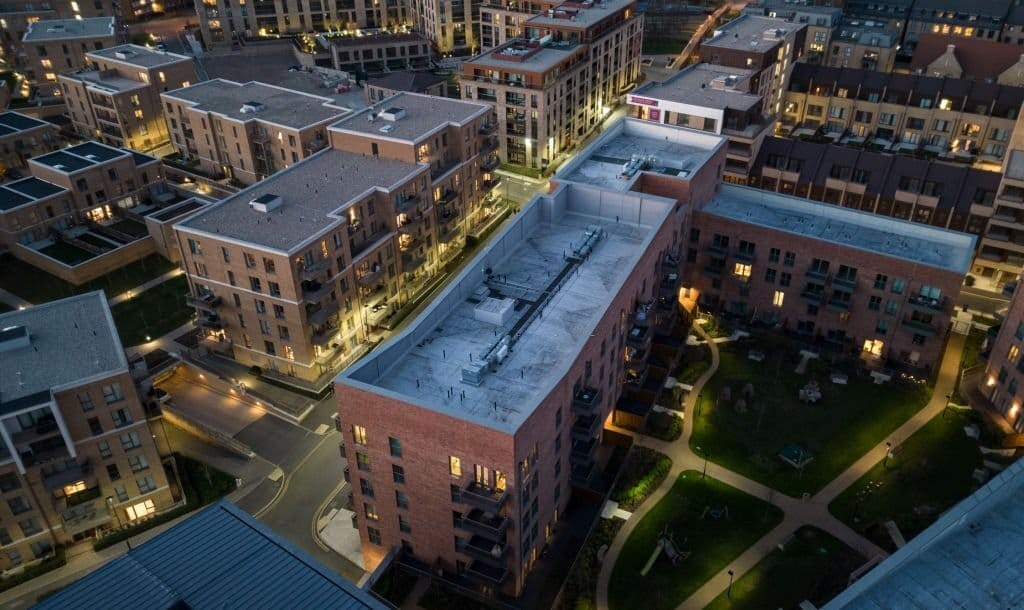 Aerial twilight view of a contemporary urban apartment complex with illuminated windows and landscaped courtyards, showcasing modern residential architecture.