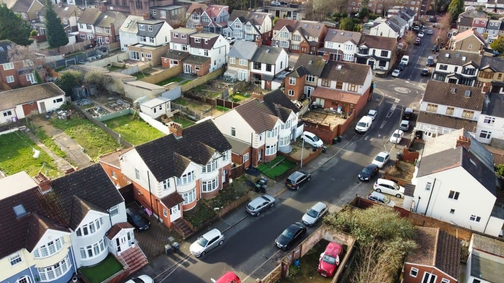 Overhead view of a typical British suburban neighborhood featuring rows of semi-detached houses with pitched roofs, private gardens, and parked cars, highlighting suburban residential planning.