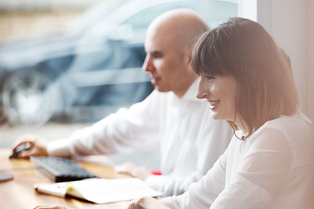 Two professional architects, a bald man and a woman with brown hair, working together at a sunlit office desk, reviewing plans and discussing project details, embodying teamwork and collaboration in urban planning.