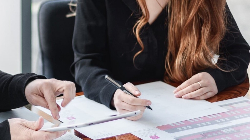 Close-up of two professionals discussing over architectural drawings, with a focus on a woman's hands holding a pen, ready to make notes or adjustments.