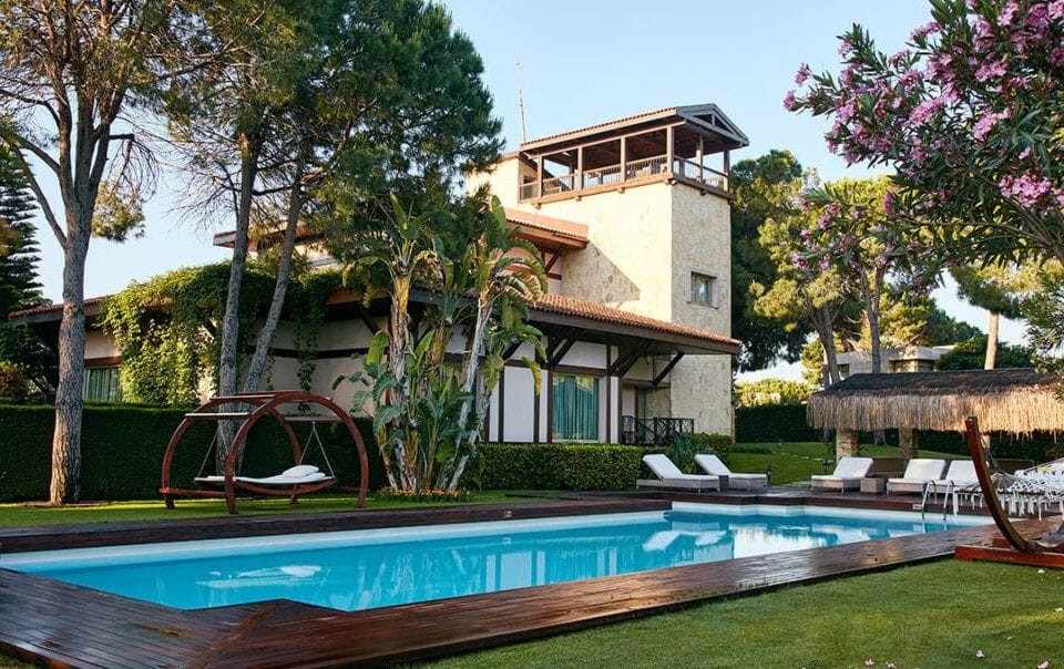 Luxurious backyard of a Mediterranean villa with a clear blue swimming pool, surrounded by a lush garden, loungers, and a unique circular swing chair, reflecting high-end residential landscape design and outdoor leisure amenities.