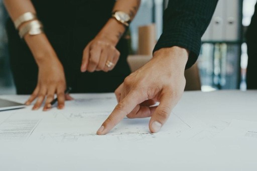 Close-up of professional hands pointing at architectural blueprint during a consultation, highlighting detail-oriented planning and design discussion.