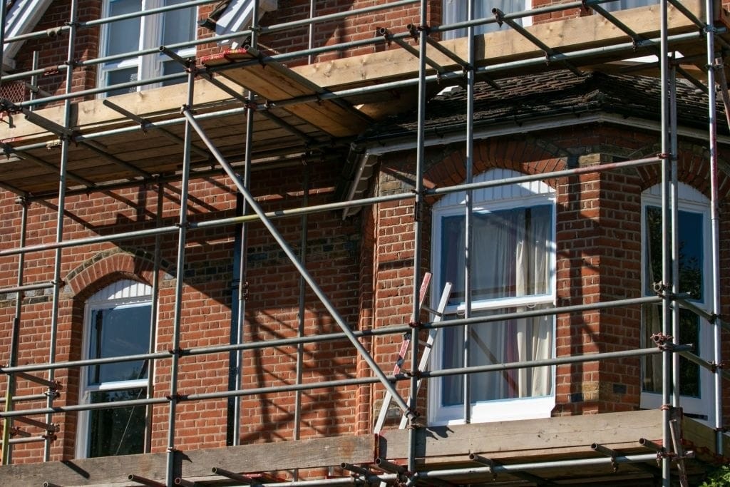 Exterior of red brick building with white windows under renovation with metal scaffolding setup on a sunny day.