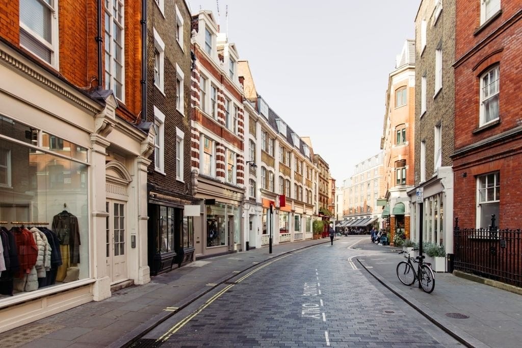 Quiet, picturesque London city street in early morning with historic architecture, showcasing a variety of storefronts and a bicycle parked on the side.