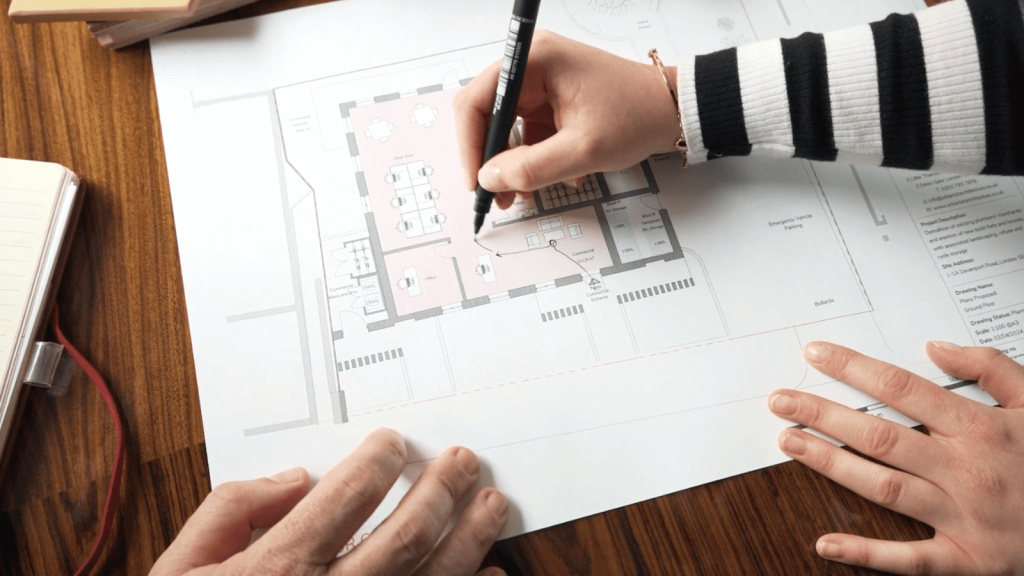 Architects marking up a building floor plan with a black marker to streamline planning permission through insightful design. The focus is on collaboration, design strategy, and planning to create effective architectural solutions.