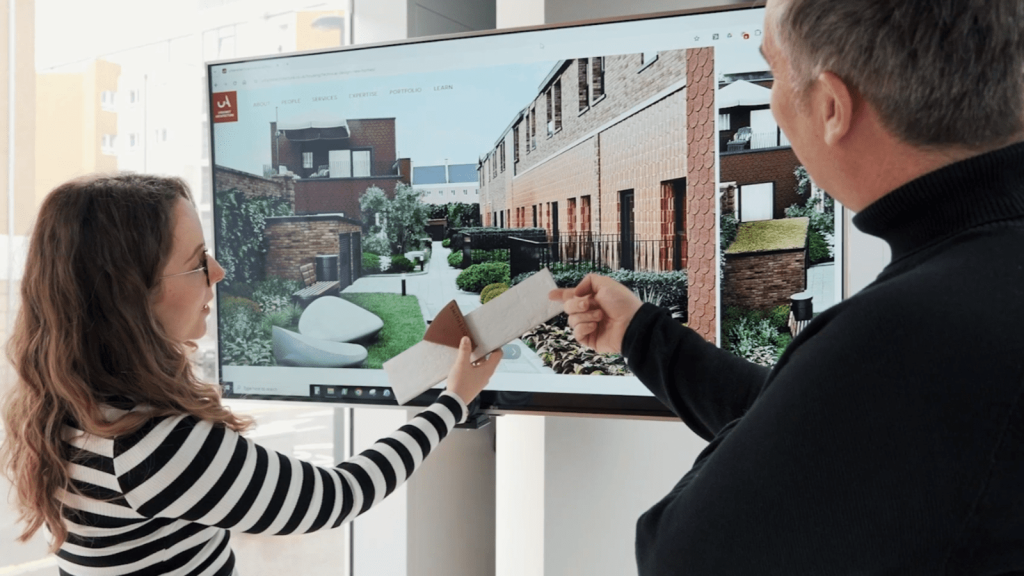 Architects discussing design plans in front of a digital display showcasing a modern residential development. They examine architectural materials and textures to highlight the importance of good design in creating value and opportunities.