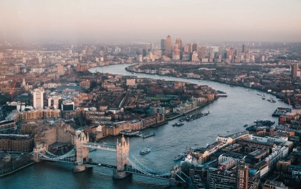 Aerial view during the sunrise on a cloudy day of the River Thames London including the famous Tower Bridge and Uber Boats travelling up to Westminster as well as view of the large skyscrapers of Canary Wharf in East London