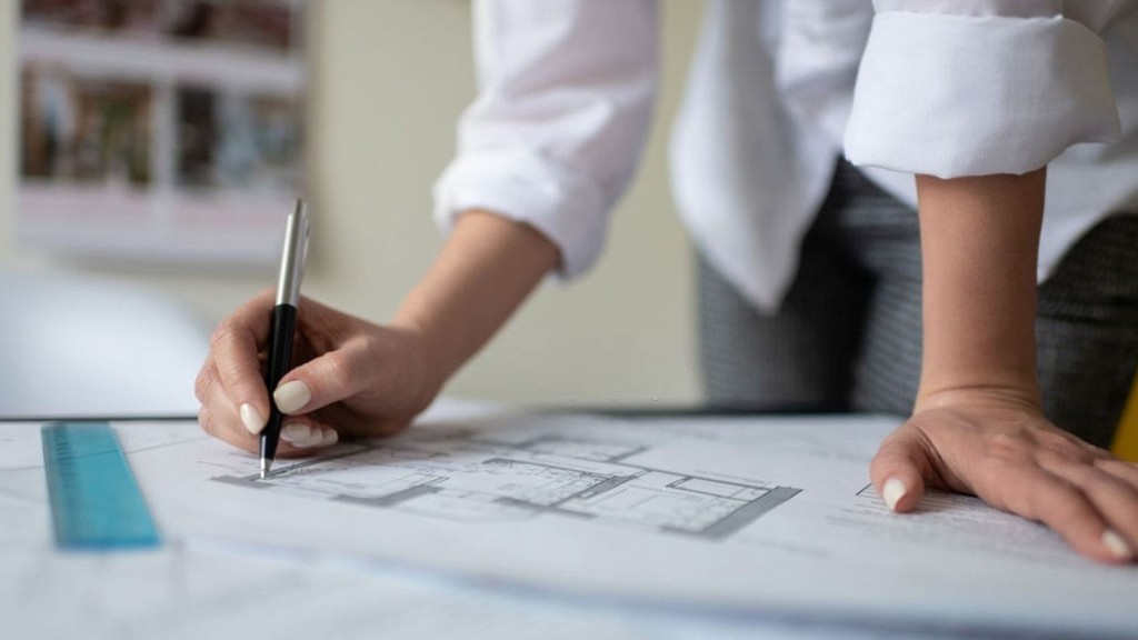 Professional architect drawing plans with a ruler and pen on architectural blueprints, focusing on a detailed construction plan.