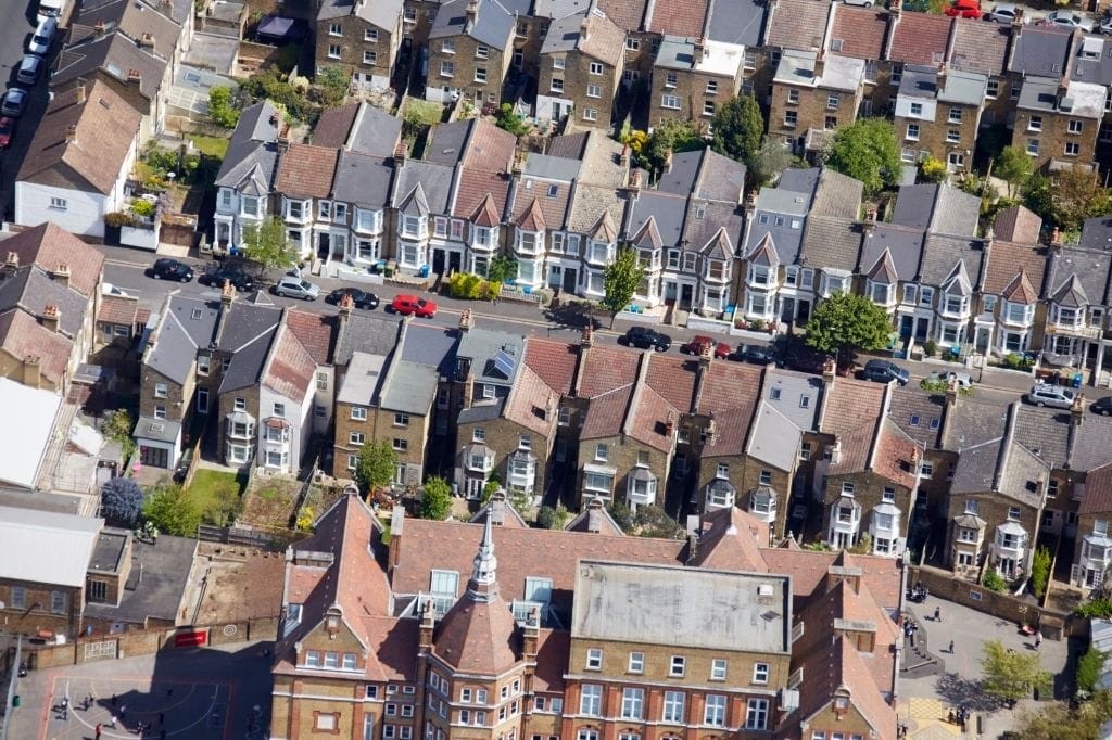 Aerial view of a dense suburban neighborhood with rows of terraced houses, distinctive bay windows, and parked cars, highlighting typical residential architecture in an urban area.