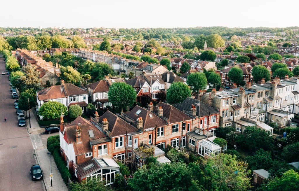 Aerial photograph on a sunny day of a residential neighbourhood and its typical streetscape of double storey houses with pitched roofs or triple storeys terrace houses with flat roofs, the majority with single or double rear extensions