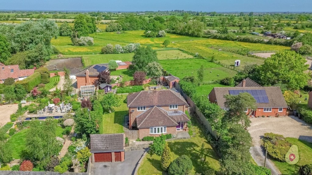 Bird's-eye view of a serene English countryside property in North London, showing a detached house with a landscaped garden and solar panels. Adjacent to the home are lush green fields with grazing animals, outlined by traditional hedgerows. This rural setting provides a stark contrast to the urban environment, emphasising the variety of property types for due diligence in the region.