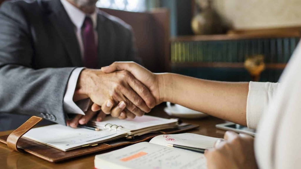 Professional handshake across a table with open notebooks, a pen, and a leather-bound planner, symbolising a successful business agreement or partnership.