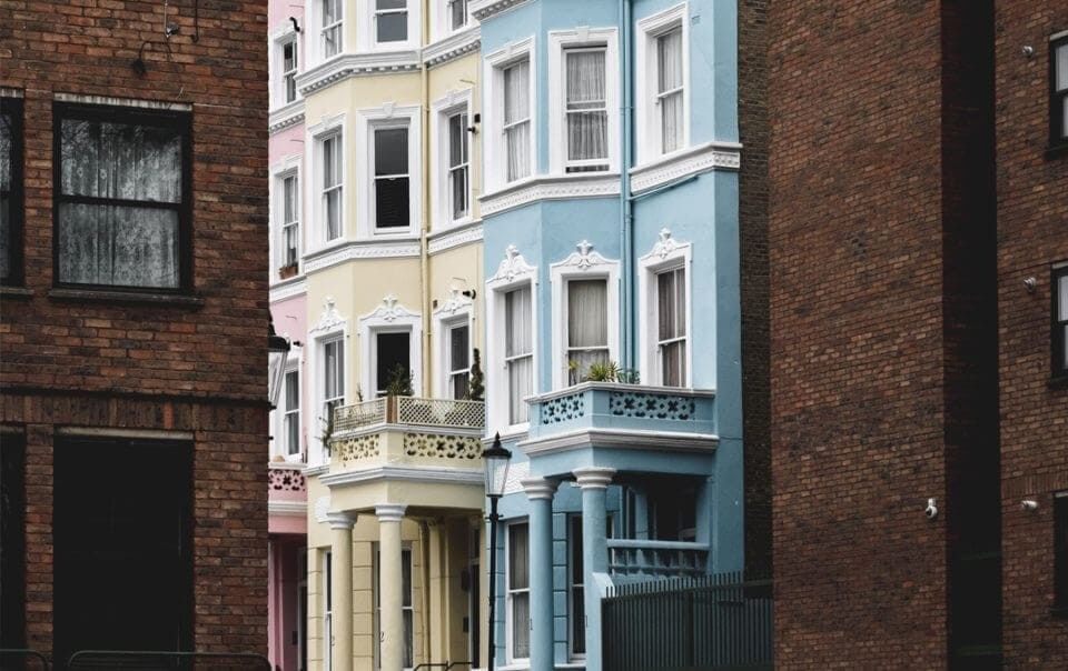 Contrasting architectural styles with a row of pastel-colored Victorian townhouses nestled between two dark brick buildings, highlighting diverse property investment options.