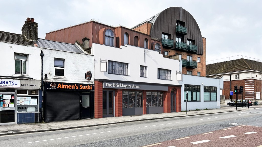 Modern-meets-traditional streetscape in Greenwich showing The Bricklayers Arms pub and sleek boutique hotel on the upper floors next to a curved roof flatted development. 