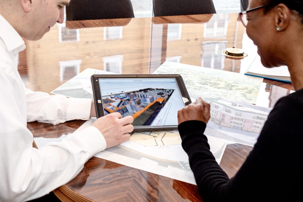 On the left is a planning consultant at Urbanist Architecture in the meeting room reviewing RIBA chartered architect's drawings on an iPad with a client on the right hand side who is smiling at the proposed designs for her investment