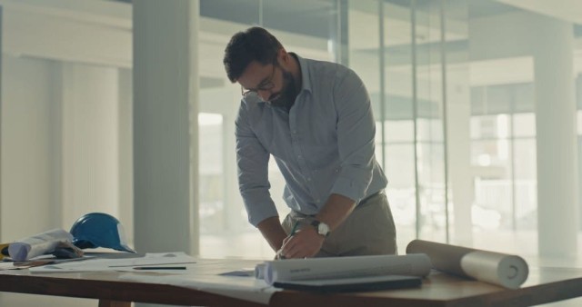 Image cover for the article: Focused young female architect with long hair drafting architectural plans, with hands visible working on a drawing with a pen, symbolising precision and attention to detail in planning and design.