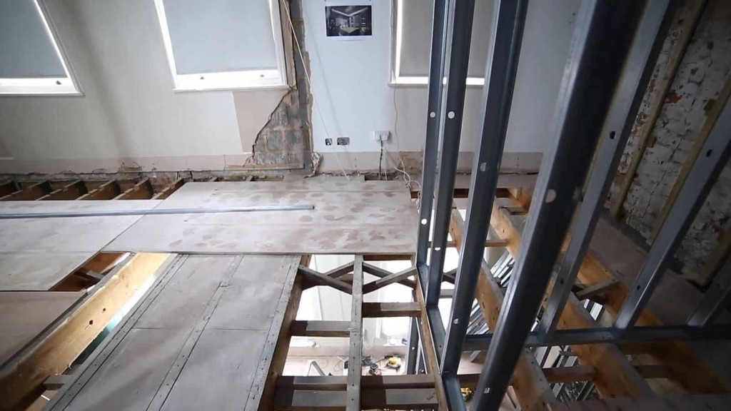 Home renovation in progress with a view of a partially deconstructed floor and metal stud partitions, showcasing the skeleton of wooden beams and the installation of new electrical wiring.