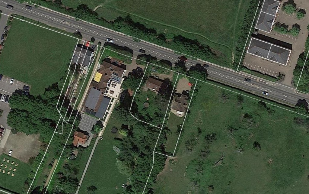 Overhead satellite view of residential property outlined for potential development next to a highway, illustrating urban planning and land use for replacement dwelling projects in a suburban setting.