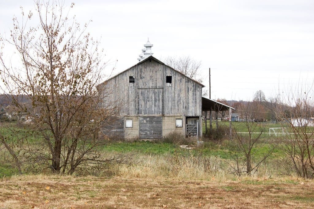 Rustic weathered wooden barn in rural setting with bare trees and overcast sky, indicative of farm life and agricultural heritage.