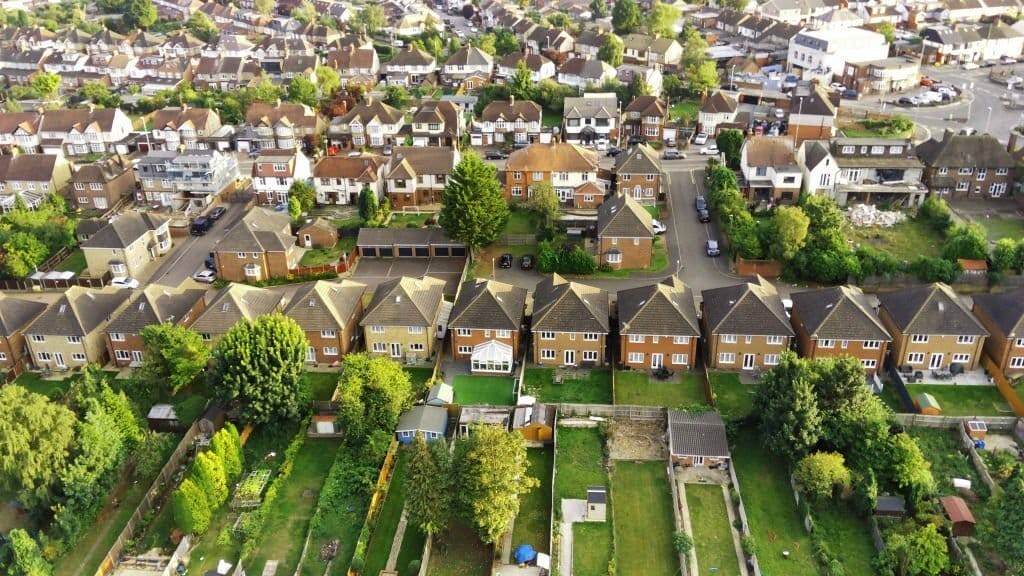 Bird's-eye view of a UK suburban neighborhood showing rows of semi-detached houses with gardens, amidst a dense arrangement of streets and homes.