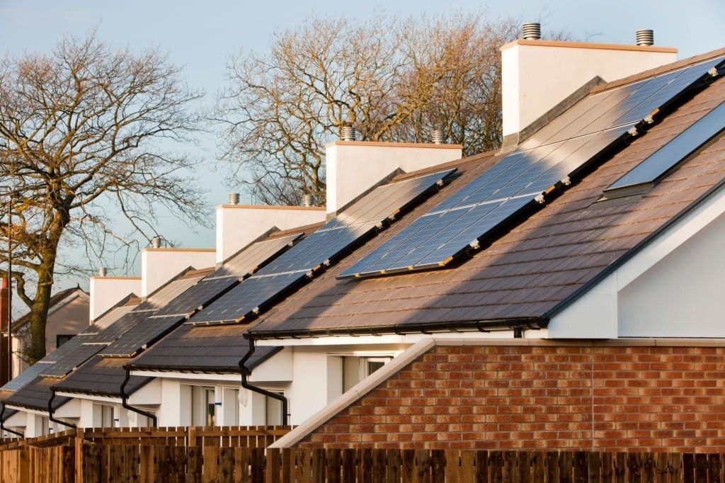 Row of new-build homes with solar panels installed on the roofs, capturing renewable energy, set against a clear sky with leafless trees in the background.