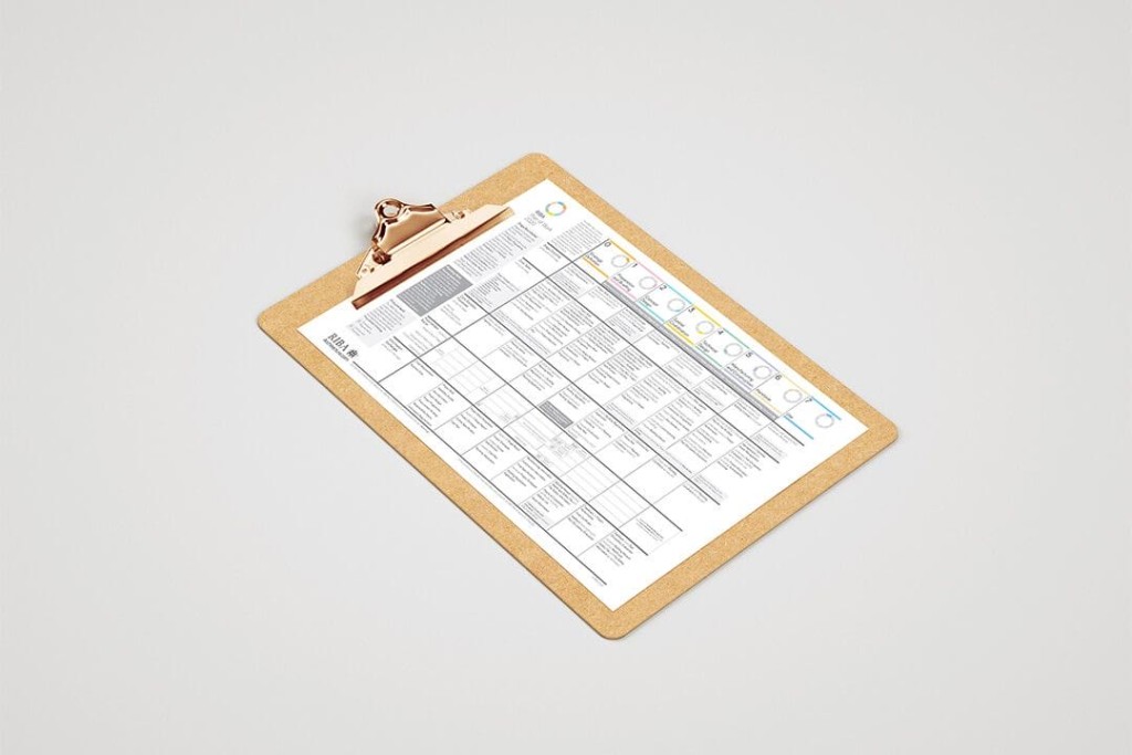 RIBA Plan of Work 2020 chart on clipboard with detailed project stages and tasks, viewed from an overhead angle on a neutral background, highlighting architectural project planning and management processes.