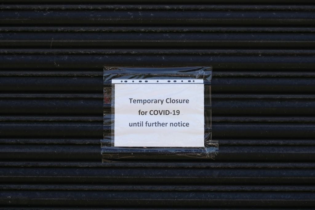 Temporary closure notice for COVID-19 taped to a dark metal shutter, highlighting the impact of the pandemic on businesses and the potential for converting vacant commercial properties to residential use under new permitted development rights in England.