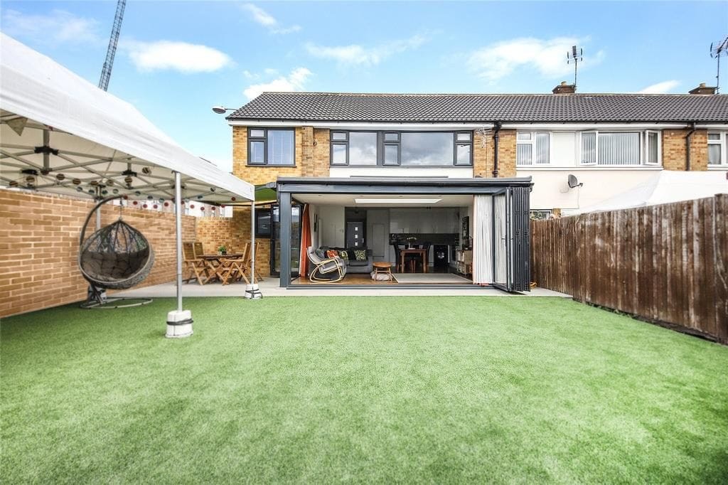 Modern house backyard with artificial grass, hanging egg chair, wooden furniture, and open patio doors leading to a stylish interior.